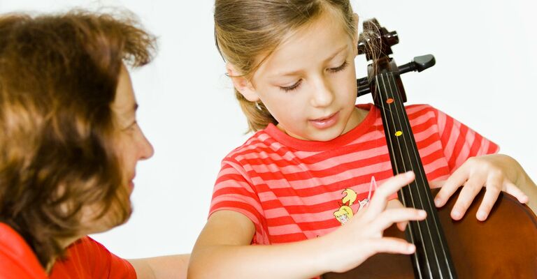 Cellolehrerin zeigt Schülerin am Cello die richtige Handhaltung